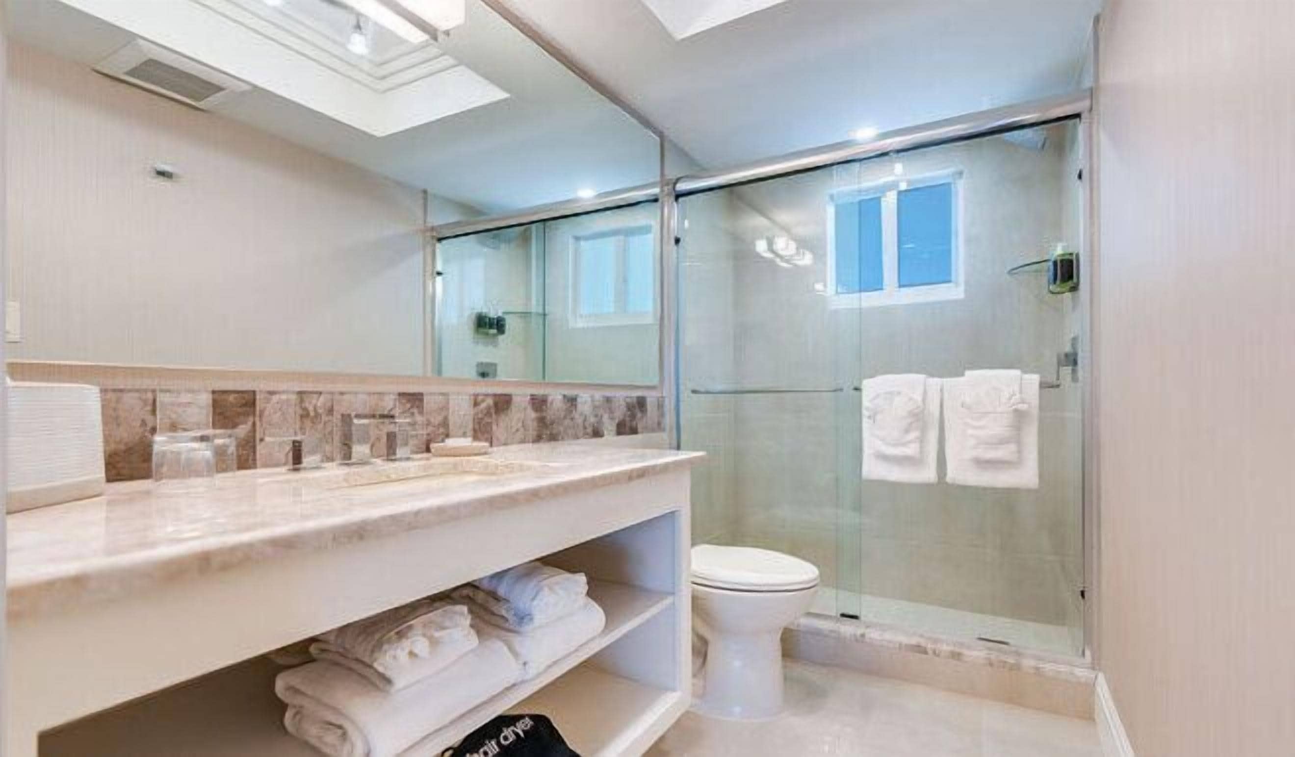 A modern bathroom with a glass shower enclosure, a marble countertop, and a toilet.