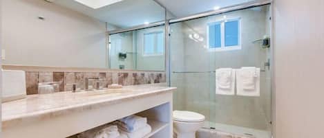 A modern bathroom with a glass shower enclosure, a marble countertop, and a toilet.
