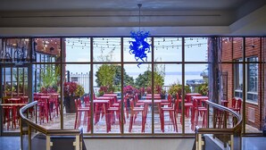A restaurant with red chairs and tables, a view of the outside, and a decorative blue sculpture. - Waterfront Hotel Downtown Burlington (Burlington)