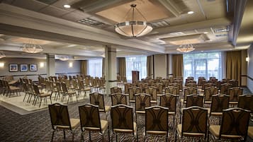 A conference room with rows of chairs, a podium, and large windows with curtains.