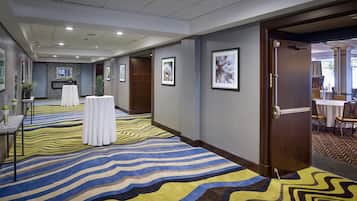 Un couloir d’hôtel avec un tapis à motifs, des œuvres d’art encadrées accrochées aux murs et un espace de restauration visible à travers une porte ouverte.