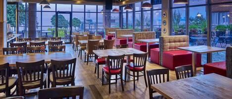 A restaurant with wooden tables and chairs, red cushioned seating, and large windows offering a view of the city.
