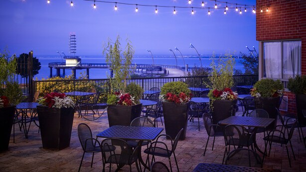 An outdoor patio with tables and chairs, string lights, and potted plants. - Waterfront Hotel Downtown Burlington (Burlington)