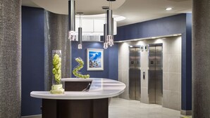A modern reception area with a curved counter, a decorative plant, a framed picture, and two elevators. - Waterfront Hotel Downtown Burlington (Burlington)