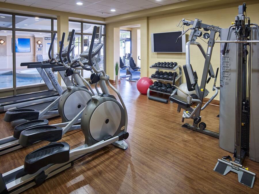 Un gimnasio con cintas de correr, elípticas, mancuernas y una máquina de remo.