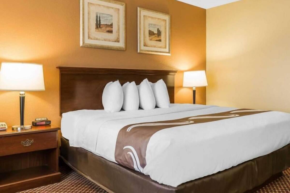 A hotel room with a large bed, two bedside lamps, a nightstand, and two framed pictures on the wall.