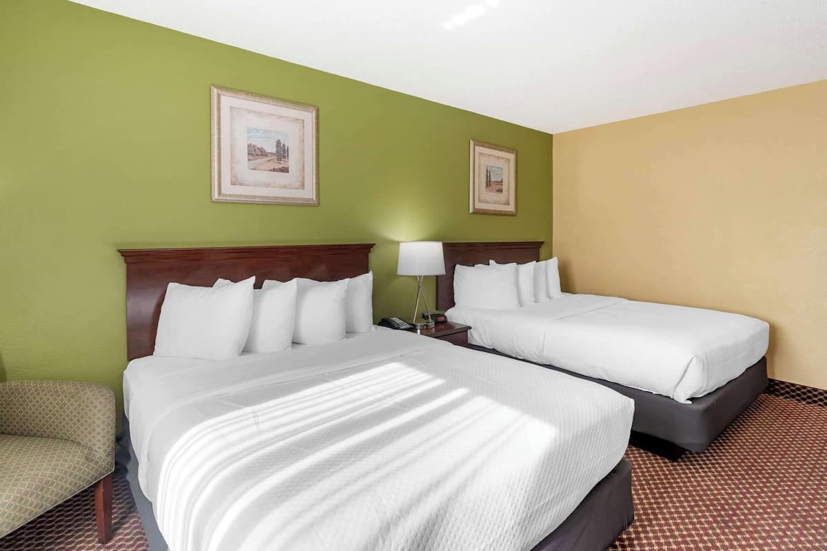A hotel room with two beds, a nightstand with a lamp, and two framed pictures on the wall.