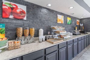 A breakfast bar with various food items, a coffee machine, and a fruit bowl.