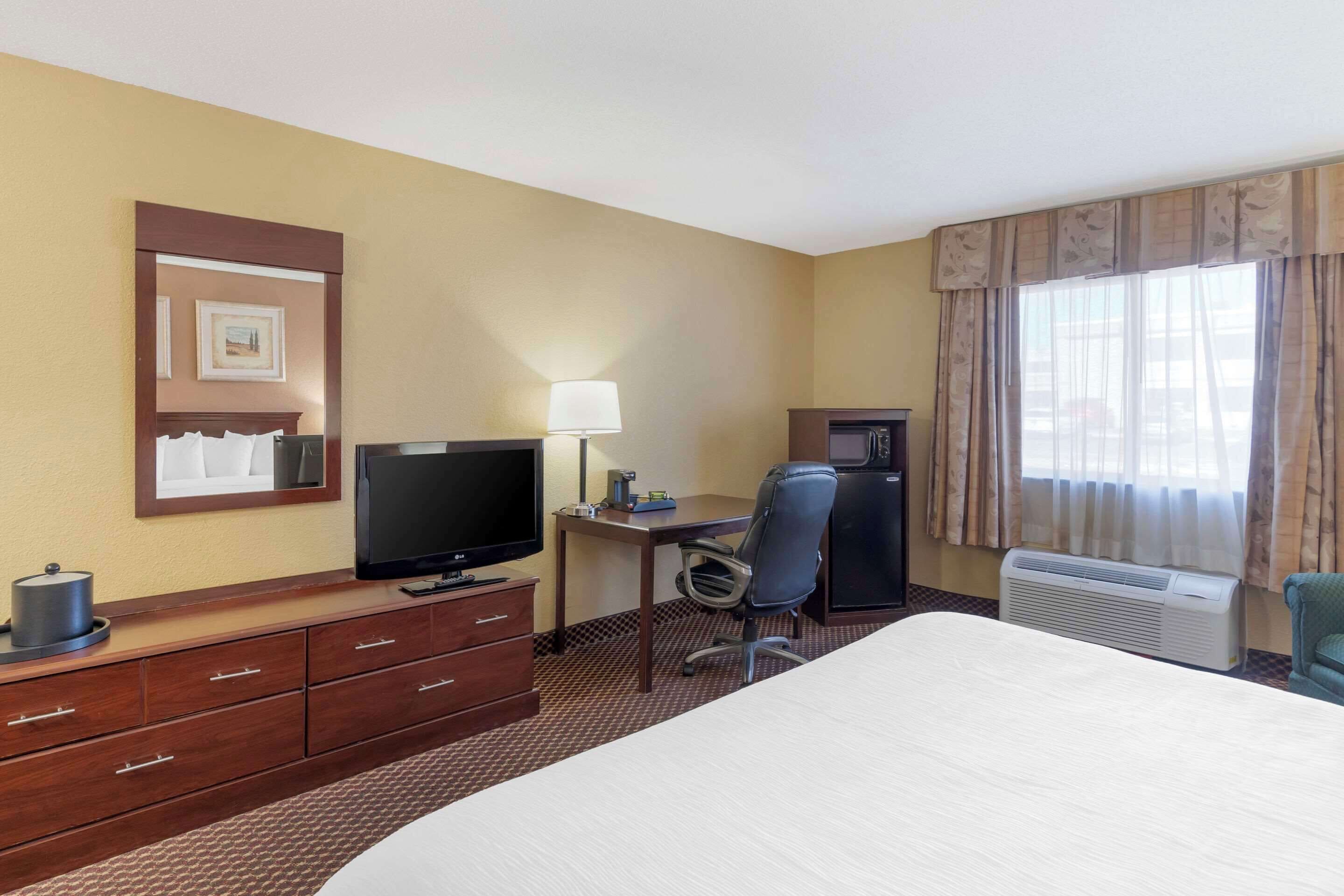 A hotel room with a bed, a desk with a computer, a television, a microwave, and a window with curtains.