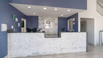 A reception desk with a 'Quality by Choice Hotels' sign, two computers, and a stone-textured counter.