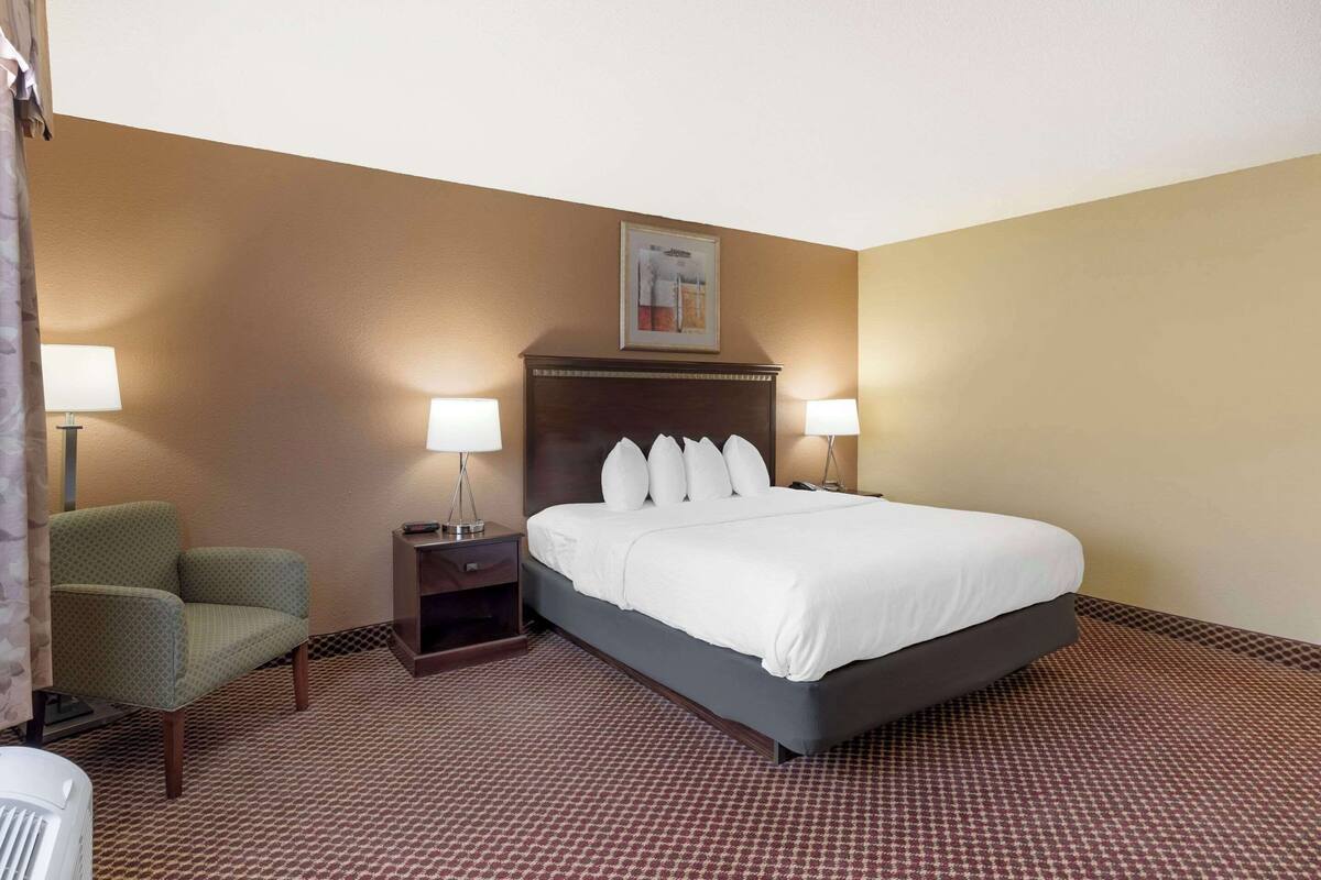 A hotel room with a large bed, two bedside tables with lamps, a green armchair, and a patterned carpet.