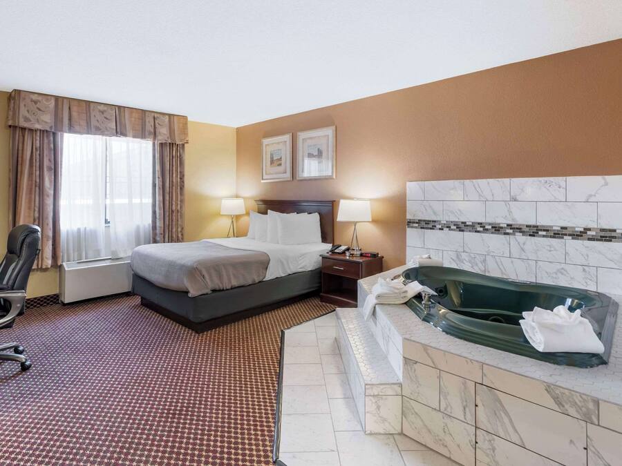 Ein Hotelzimmer mit Bett, Schreibtisch, Stuhl und einem Badezimmer mit Badewanne und Dusche.