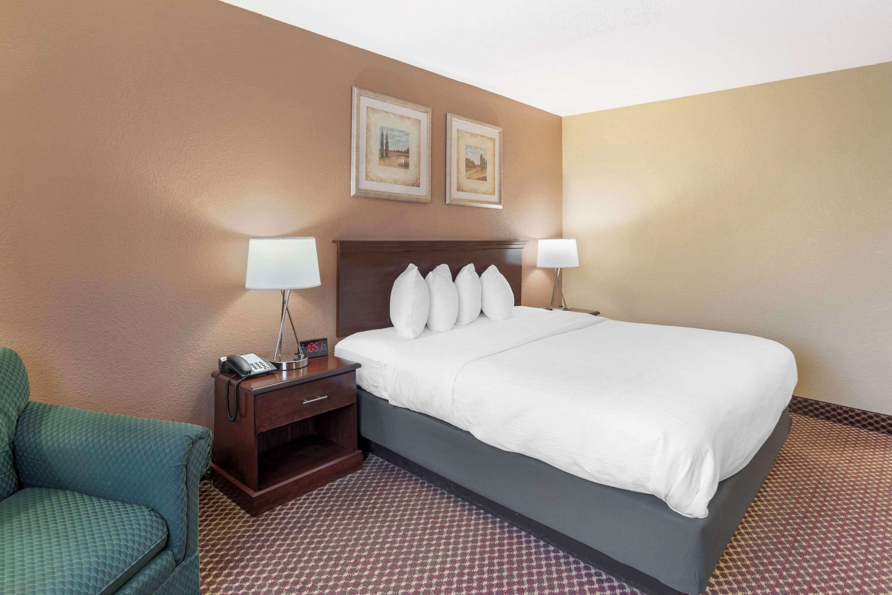 A hotel room with a bed, two bedside lamps, a telephone, a chair, and two framed pictures on the wall.