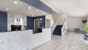 A reception area with a 'Quality' sign, a reception desk, a staircase, and a dining area with chairs and tables.