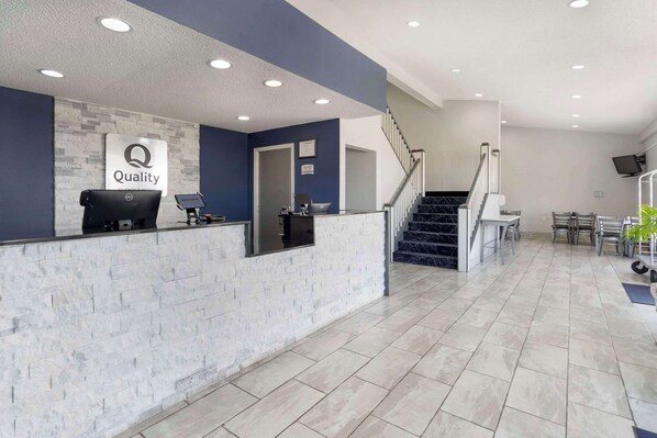 A reception area with a 'Quality' sign, a reception desk, a staircase, and a dining area with chairs and tables.
