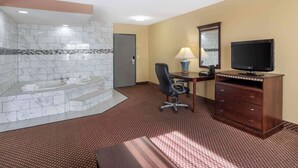 A hotel room with a marble bathroom, a desk with a chair, a television, and a dresser.