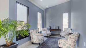 A room with a large window, a potted plant, patterned armchairs, a small table, and a rug.
