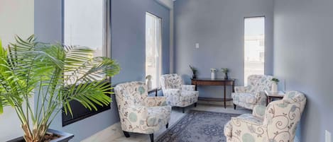 Une pièce dotée d’une grande fenêtre, d’une plante en pot, de fauteuils à motifs, d’une petite table et d’un tapis.