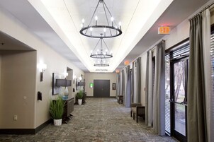 A hotel corridor with chandeliers, a reception desk, potted plants, and an exit sign.