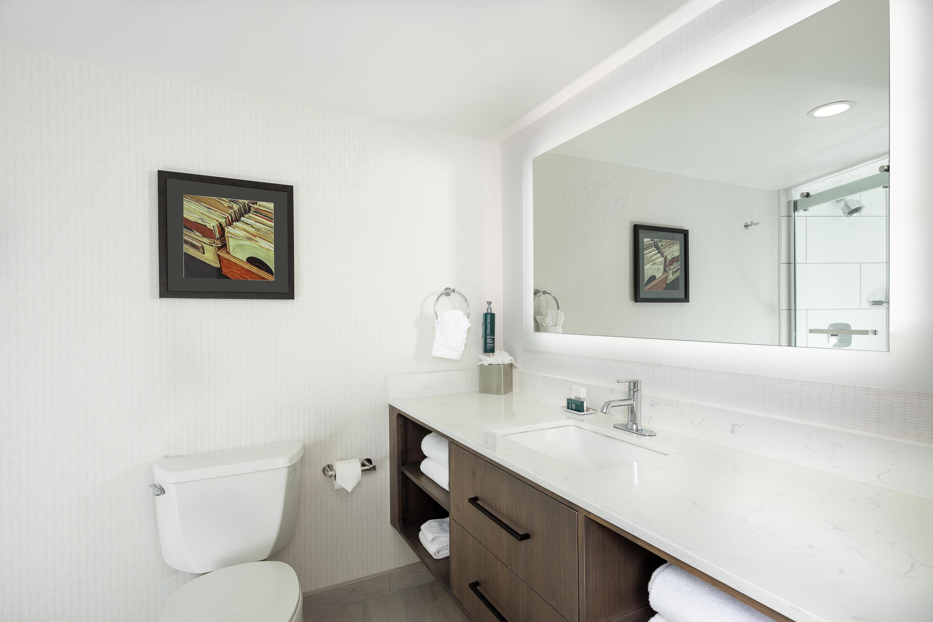 A modern bathroom with a white toilet, a sink with a mirror, and two framed pictures on the wall.