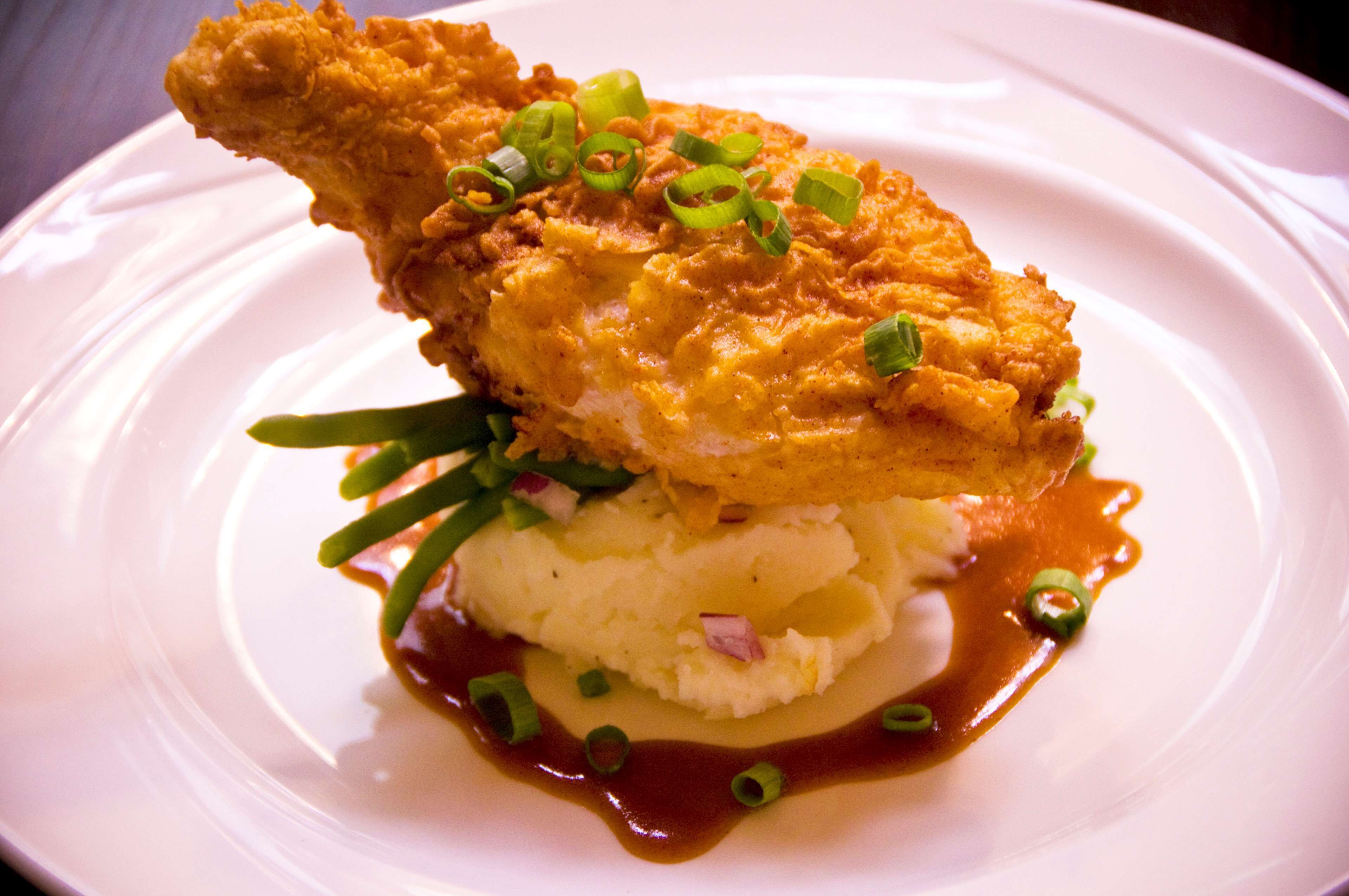 A plate with a fried chicken leg, mashed potatoes, and green onions.