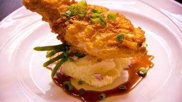 Un plato con un muslo de pollo frito, puré de papas y cebollines.