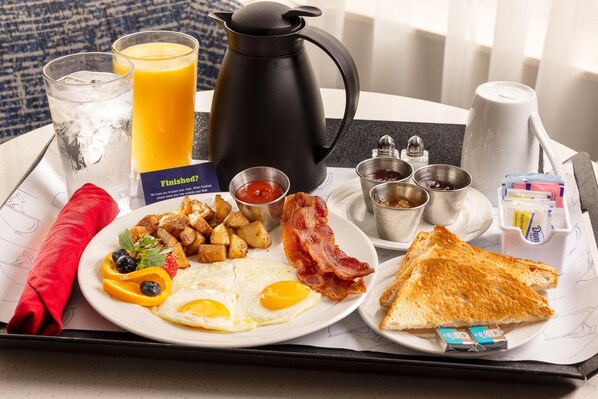 A breakfast tray with eggs, bacon, toast, potatoes, and juice.