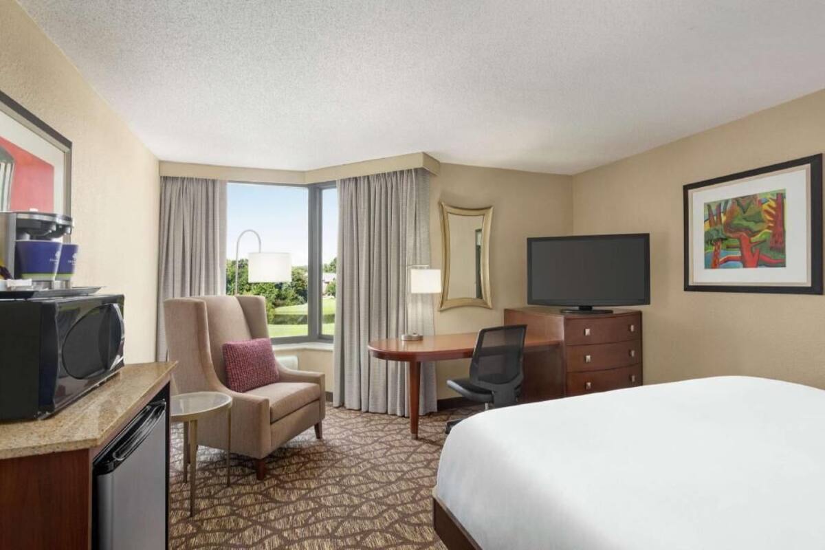 A hotel room with a bed, a desk, a chair, a television, a microwave, and a window with curtains.