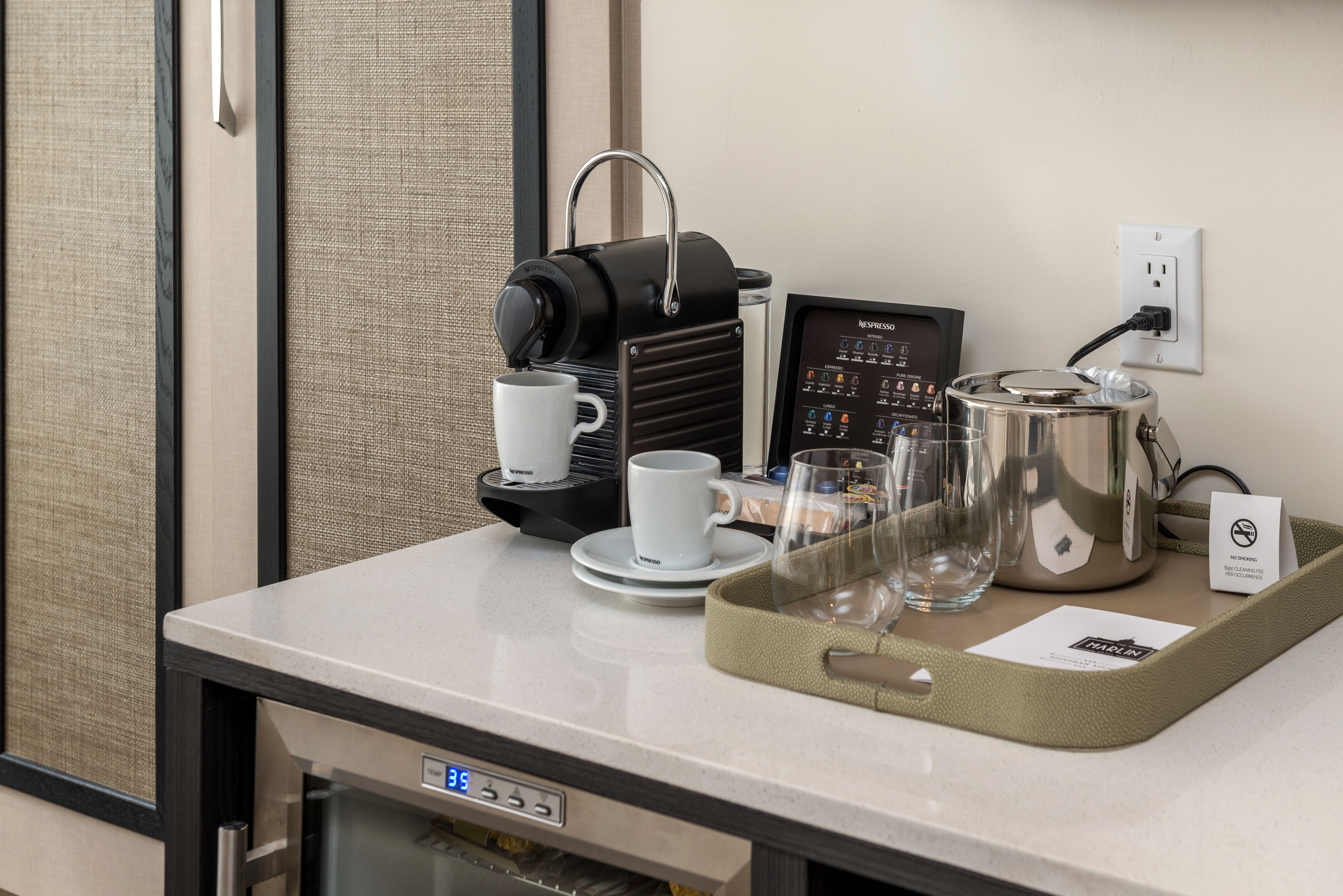 Une machine à café, une tasse, un verre et un plateau avec une cafetière, le tout posé sur le comptoir d’une chambre d’hôtel.