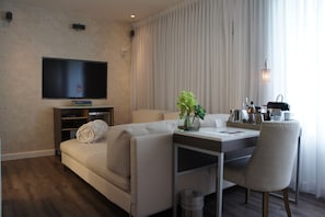 A modern living room with a flat-screen TV, a sofa, a dining table with chairs, and a small plant.
