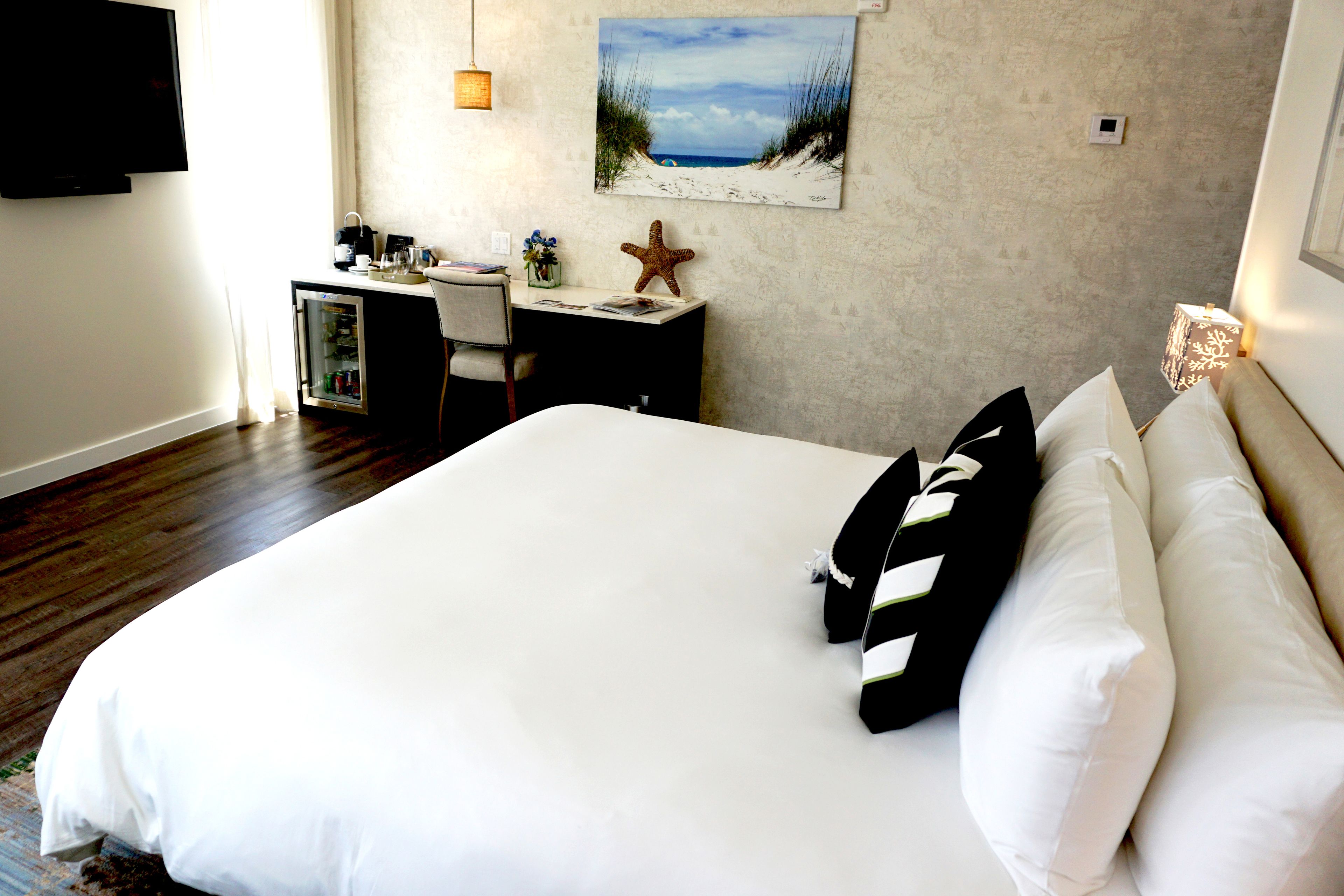 A hotel room with a large bed, a desk with a computer, a starfish decoration, and a painting of a beach scene.