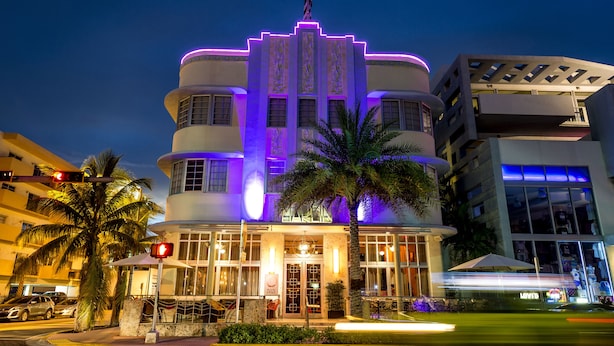 Un hotel amb una façana d'estil Art Deco característica, grans finestres i una palmera al primer pla.