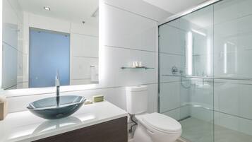 A modern bathroom with a glass-enclosed shower, a white toilet, and a large mirror above a vessel sink.