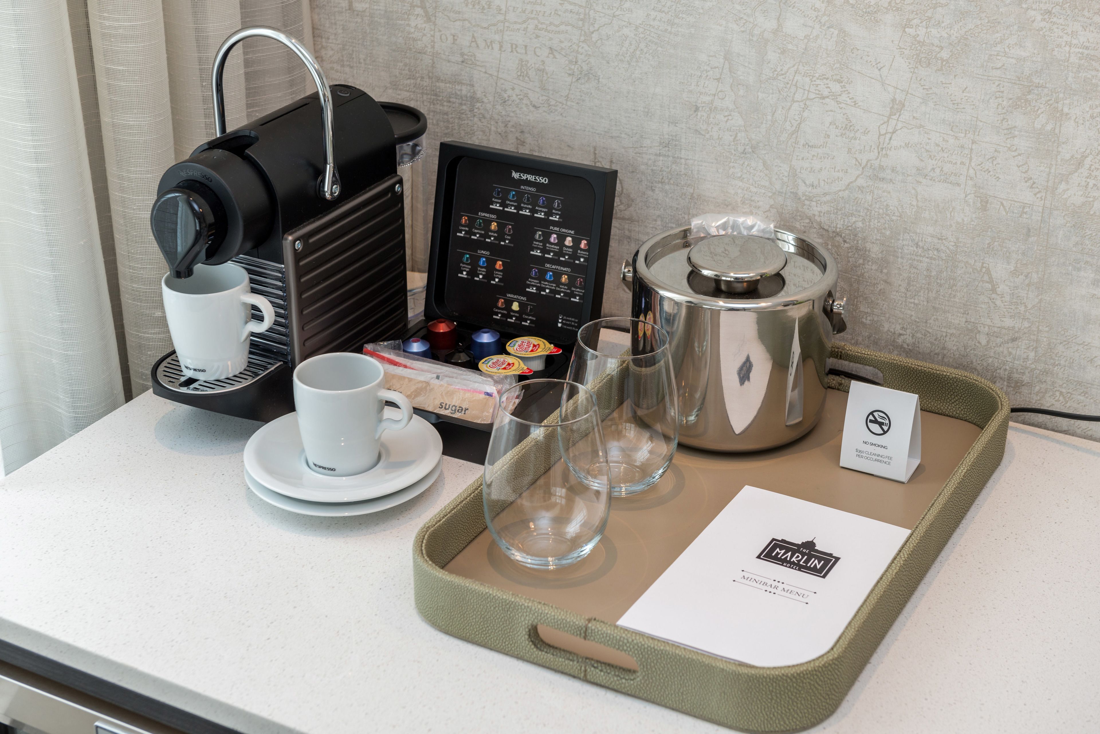 A coffee station with a Nespresso machine, cups, glasses, and a tray with a menu.