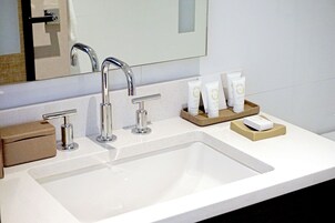 A bathroom with a white sink, two faucets, and a mirror. There are toiletries on the counter.