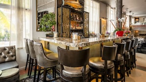 Zona de bar amb taulell de marbre, diversos tamborets i un peix decoratiu penjat a la paret.