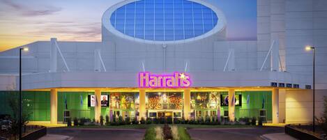 Un bâtiment moderne doté d’une grande verrière circulaire et d’un panneau lumineux au néon sur lequel on peut lire le mot « Harrah’s ».