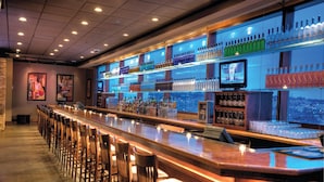 Un bar con una barra larga, varias estanterías llenas de botellas y una pantalla de televisión.