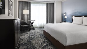 Habitación de hotel con una cama grande, un escritorio, una silla, una lámpara y vistas a la montaña a través de la ventana.