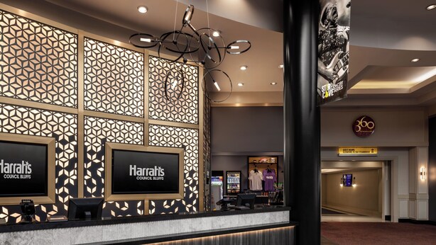 Zona de recepción de hotel con un diseño moderno, que incluye una pared estampada, un mostrador de recepción y un letrero para habitaciones de huéspedes.