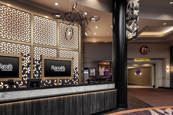 Zona de recepción de hotel con un diseño moderno, que incluye una pared estampada, un mostrador de recepción y un letrero para habitaciones de huéspedes.