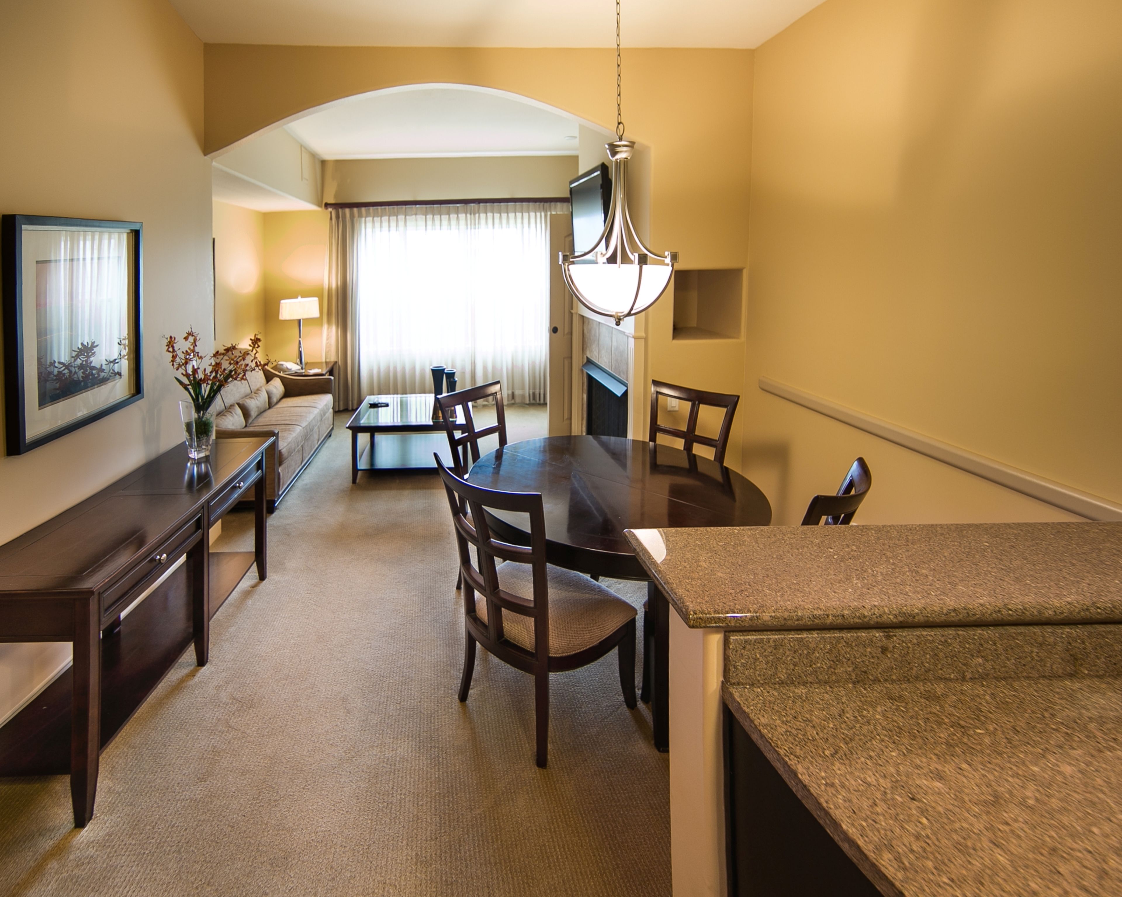 A hotel room with a dining area, a sofa, a TV, and a chandelier.