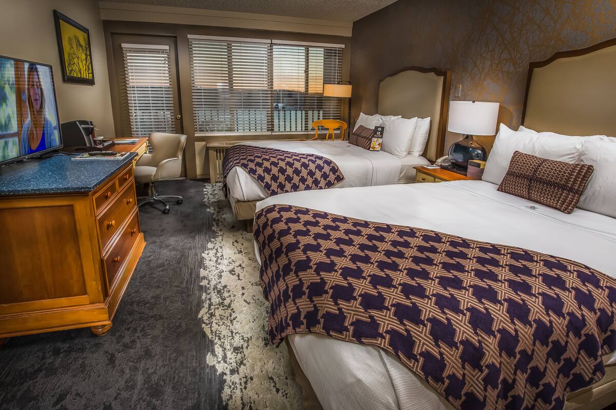 Une chambre d’hôtel avec deux lits, un bureau avec un ordinateur, une chaise et un téléviseur.