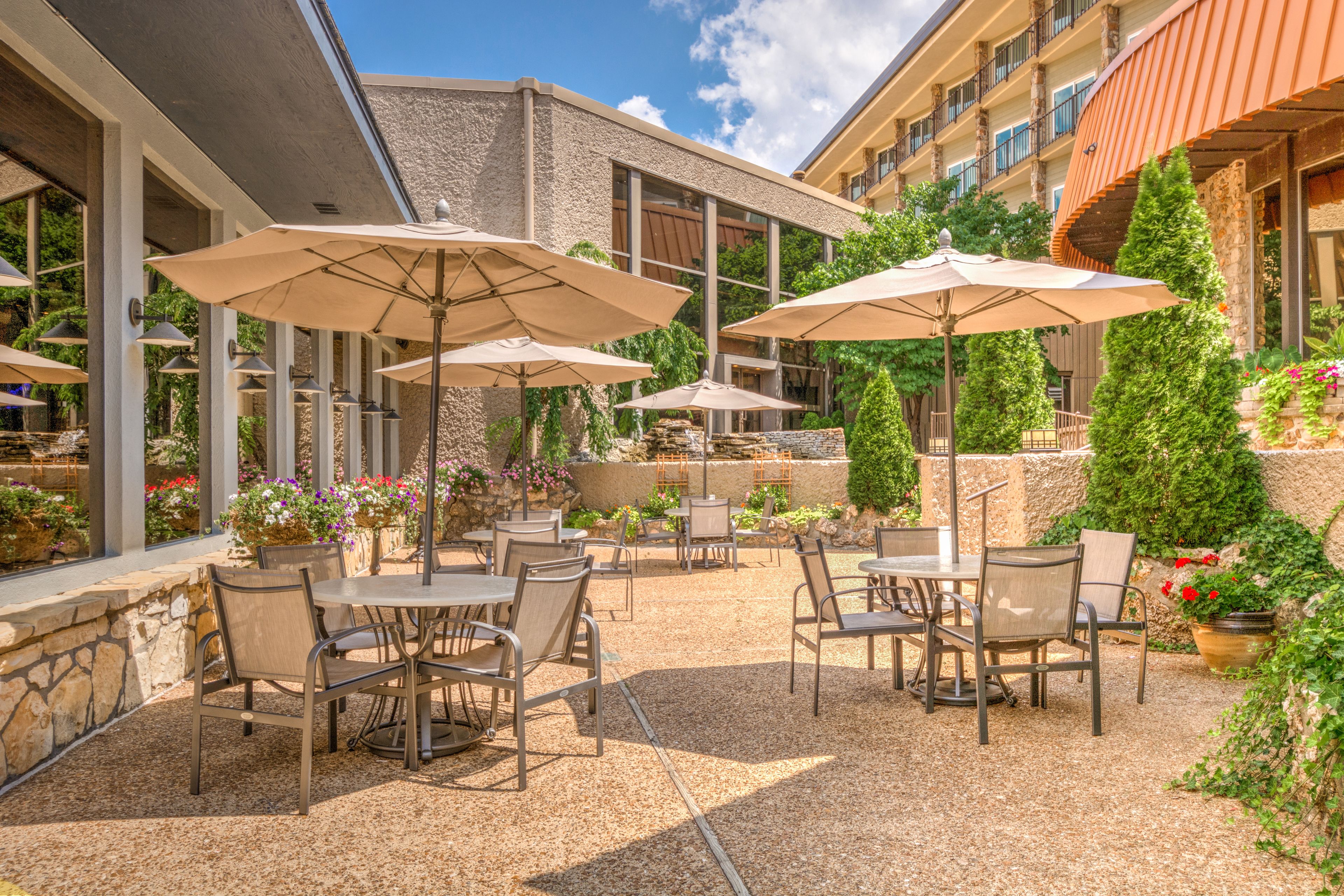 An outdoor patio area with tables and chairs, umbrellas, and potted plants.