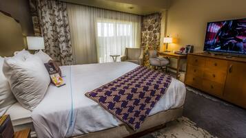 A hotel room with a large bed, a desk, a television, and a stone accent wall.