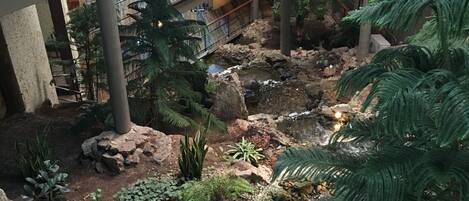 Een binnentuin met een kleine waterval, omringd door diverse planten en rotsen.