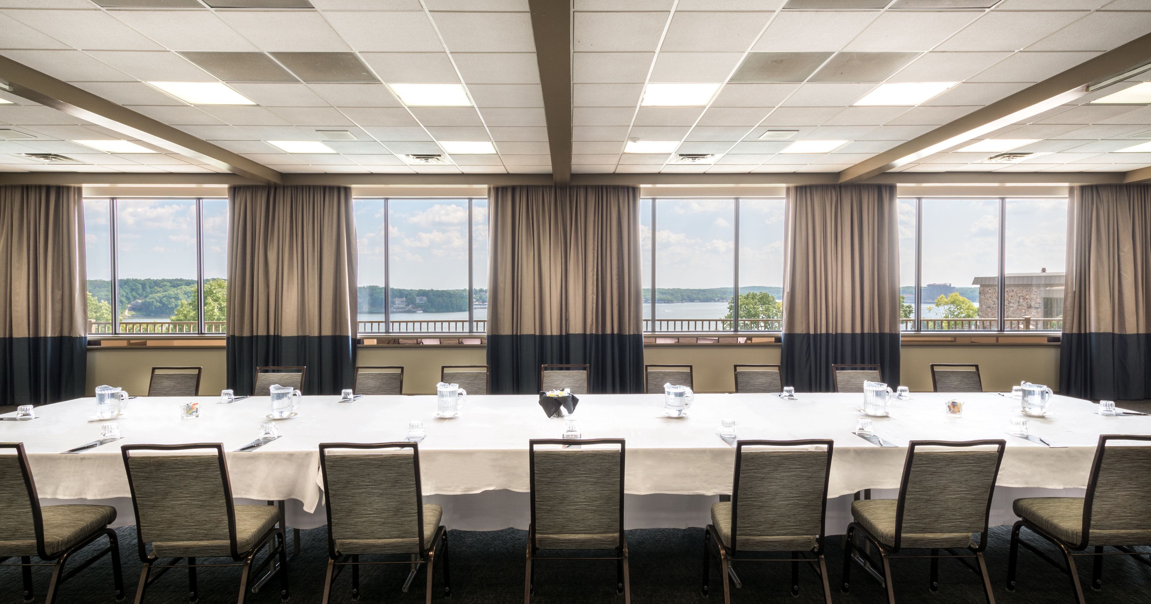 A conference room with a long table, chairs, and large windows with curtains.