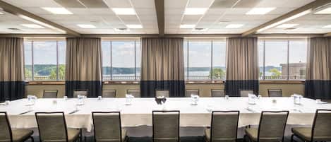 A conference room with a long table, chairs, and large windows with curtains.