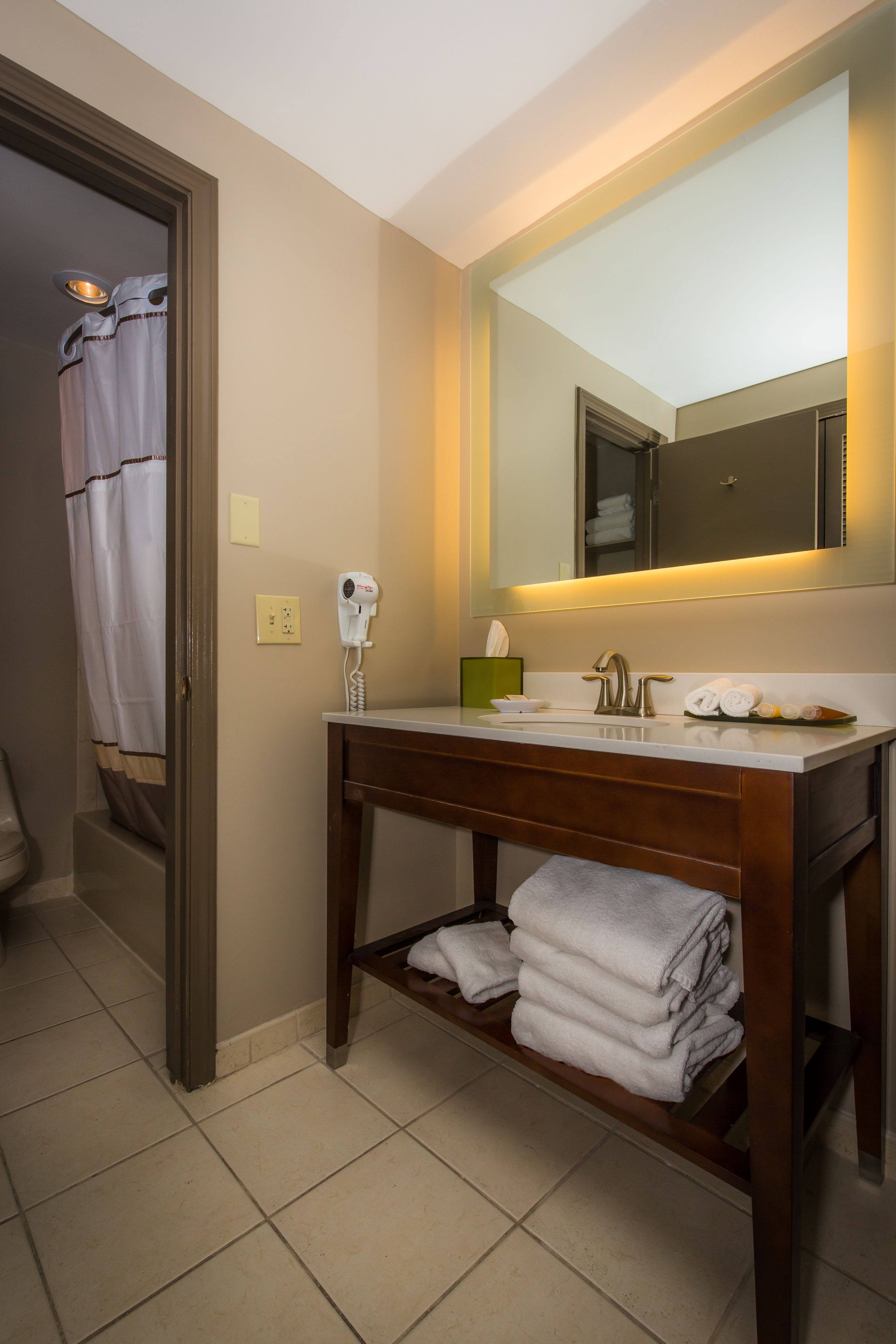 A bathroom with a vanity, a hairdryer, a mirror, and towels.