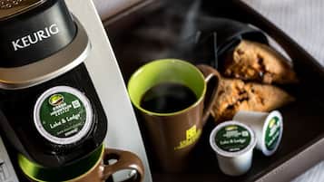 A Keurig coffee maker with a green Mountain Coffee logo, a brown mug, a green mug, and two small containers of coffee.